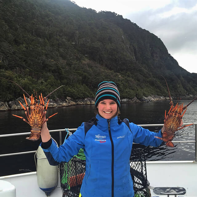 Young female in a blue jacket proud to be holding two crayfish onboard the Southern Secret in Doubtful Sound.